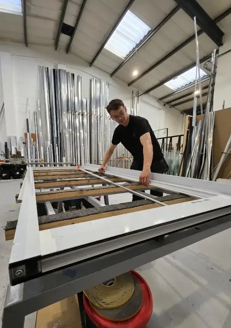 Technician beading a glazed aluminium door on the workshop jig table